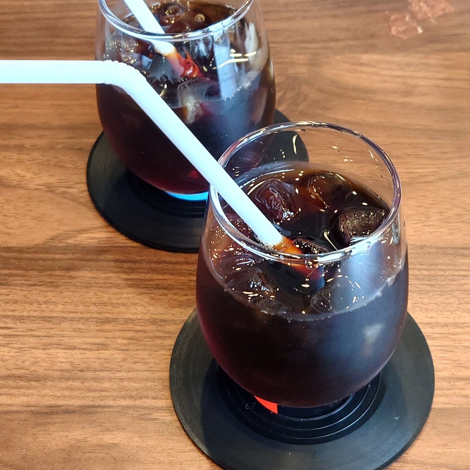 木製テーブルにレコード盤コースターで並んだアイスコーヒー2杯と白いストロー
